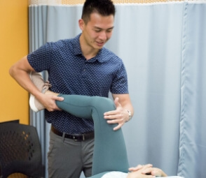 Physiotherapist performs manual therapy on the knee of a female patient as she lies on a clinic table.