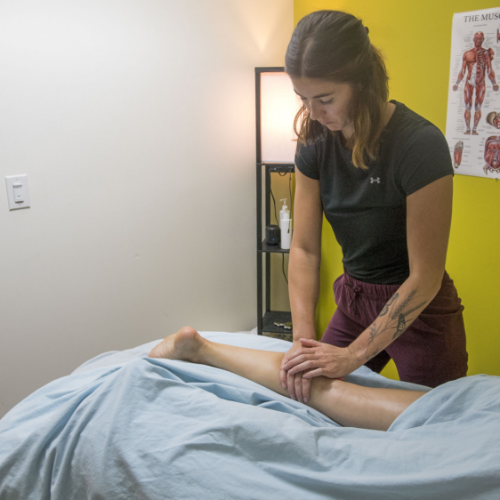 Therapist massages the calf of a patient lying face down on clinic massage table.