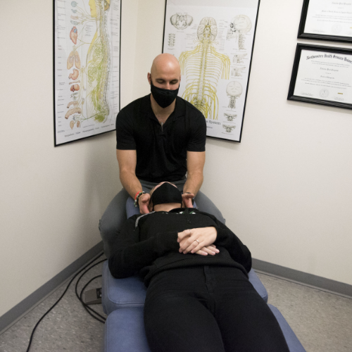 Patient is lying on her back on a chiropractic table as chiropractor performs treatment on her neck and head for pain relief.