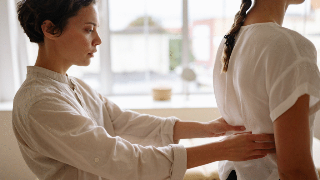 A woman practitioner checks on a female patient's mid-back in a clinical setting.